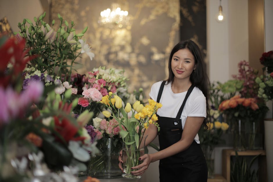 A vibrant outdoor flower stall featuring an array of freshly arranged blooms, including red and white roses, chrysanthemums, and various seasonal flowers, all displayed in white buckets and on shelves