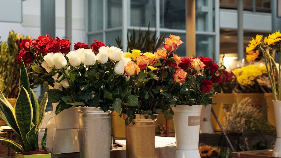 A professional florist from Kingston Florist is handing a bouquet of fresh pink roses, with tightly closed petals and green stems, to a customer through a glass display window. The bouquet is wrapped